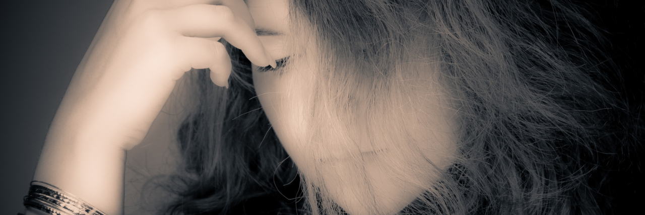 What I Want My Loved Ones to Know About My Chronic Fatigue Syndrome A photo of a woman with her forehead resting on her face.