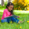Girl sitting in the grass reading a book.