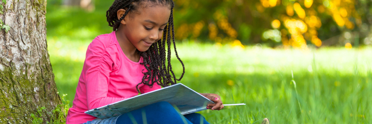 Girls Can Have Autism, Too Girl sitting in the grass reading a book.