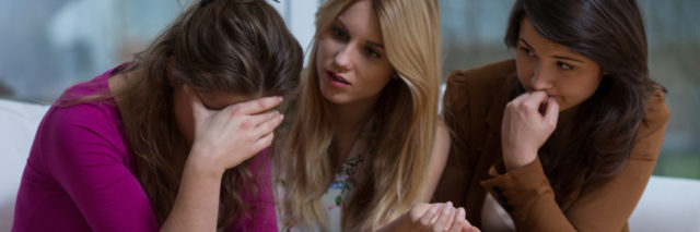two young women talking to third female friend upset