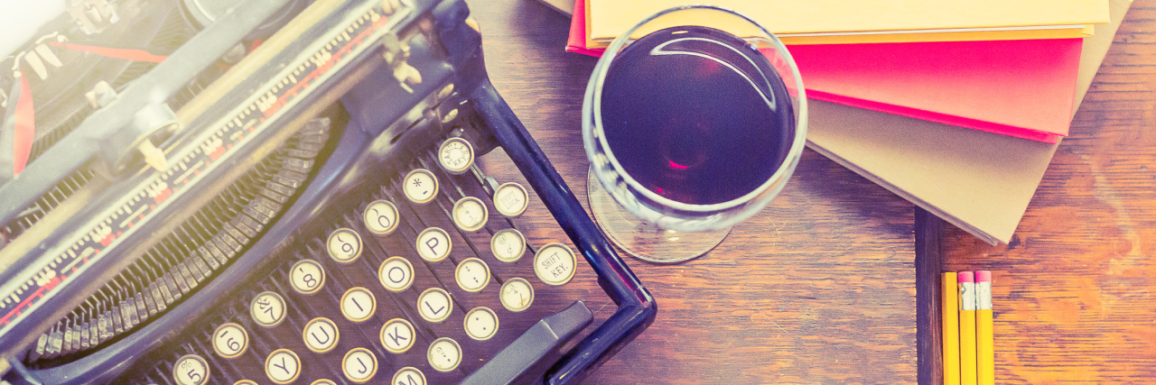 A vintage typewriter with paper, pencils, and a glass of wine next to it.