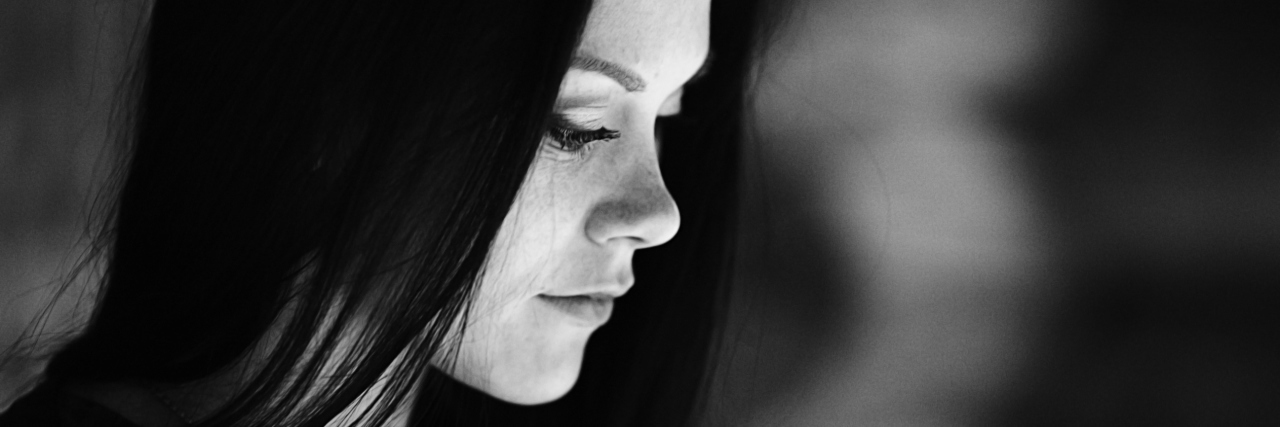 Why We Need to Have Compassion for People With Chronic Illnesses A black and white photo of a woman, looking down with a serious expression.