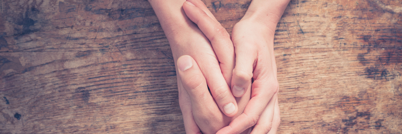Six Months On, How Am I Handling the Death of My Brother? Two people holding hands on wooden table in comforting gesture