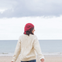 rear view of woman wearing hat and sweater, walking on beach on a cloudy day