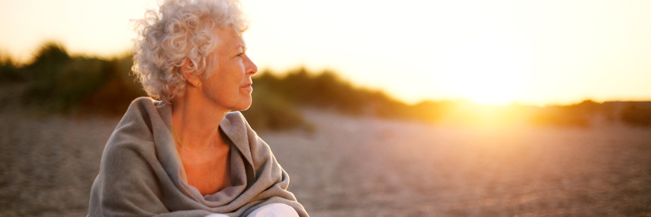 Practicing Patience to Cope With Stress of Chronic Illness older woman sitting on a beach at sunset