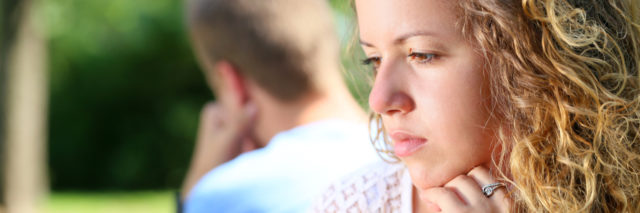 young couple with focus on woman looking sad and boyfriend behind her out of focus