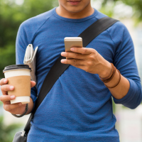 Man with coffee in his hand, while looking at his cell phone.