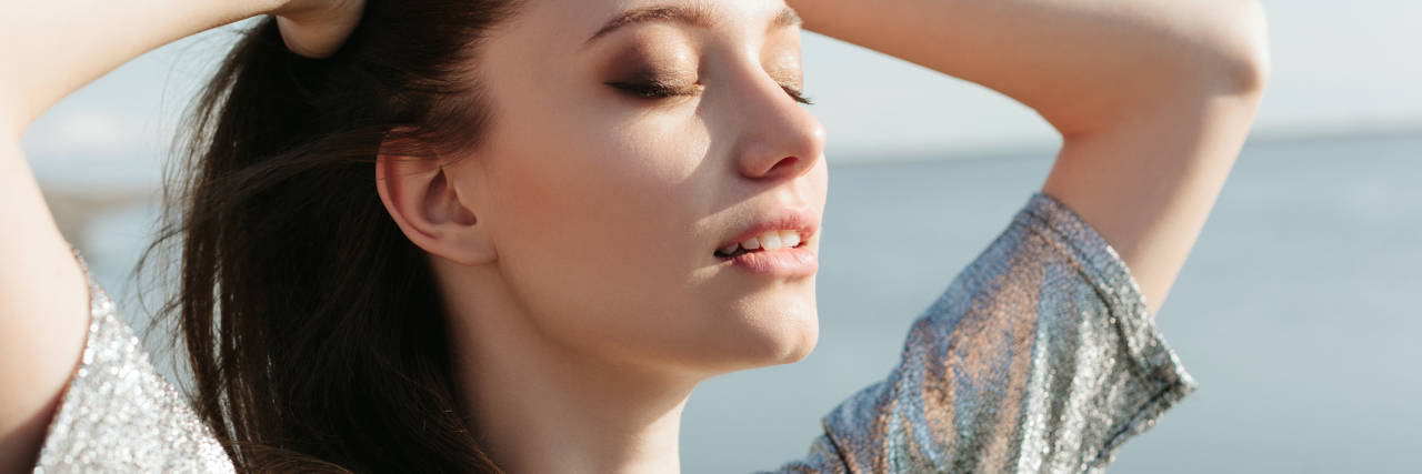 Why I'm Thankful for How Crohn's Disease Has Changed Me woman standing by the ocean with her hands on her head