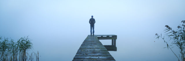 man standing alone on jetty on lake on foggy day