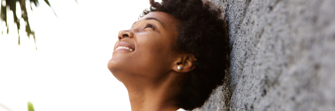 Feeling Thankful for Pseudotumor Cerebri and Epilepsy woman leaning against a wall, looking up and smiling