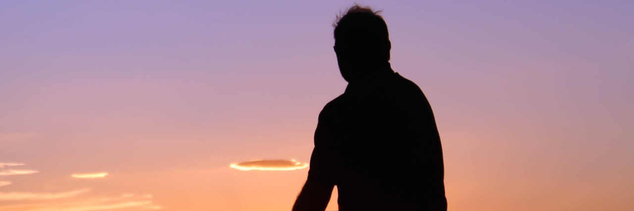 Why It's Important to Talk About Grief Silhouette of man sitting on rock, facing sunset sky