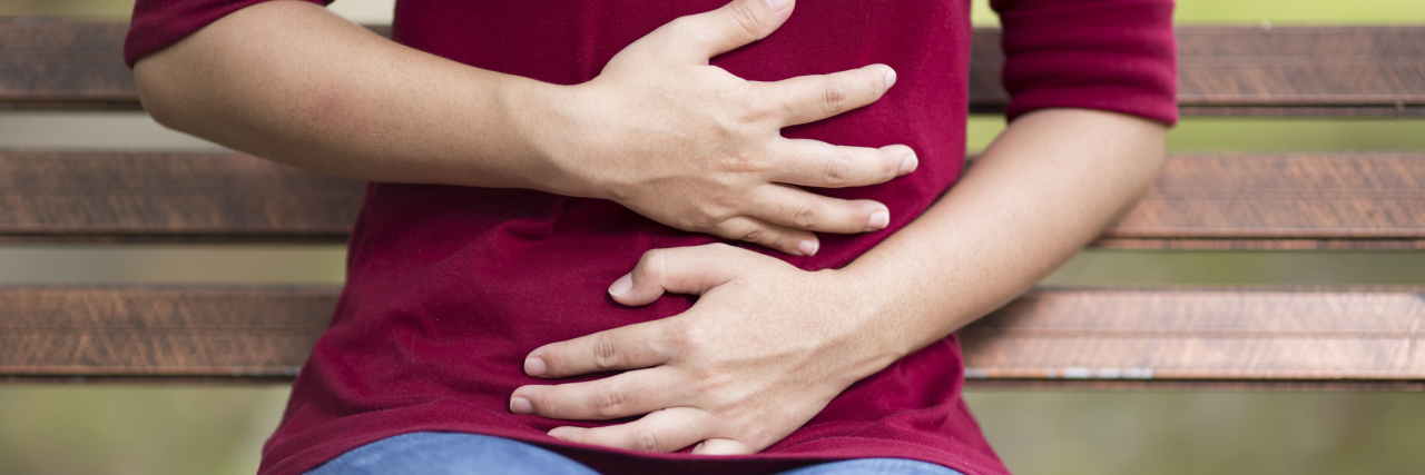 Why Emetophobia Is So Much More Than Hating Being Sick woman on park bench with stomach ache