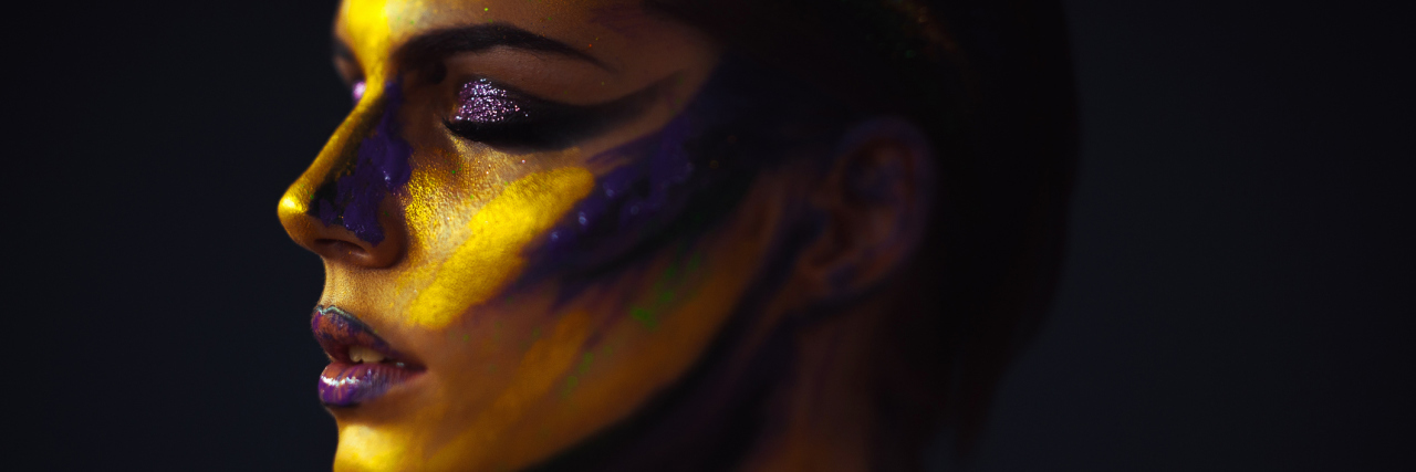 Just Because I'm Smiling Doesn't Mean I'm Well A woman with body art on her face and shoulders, with her eyes closed and a tired expression on her face.