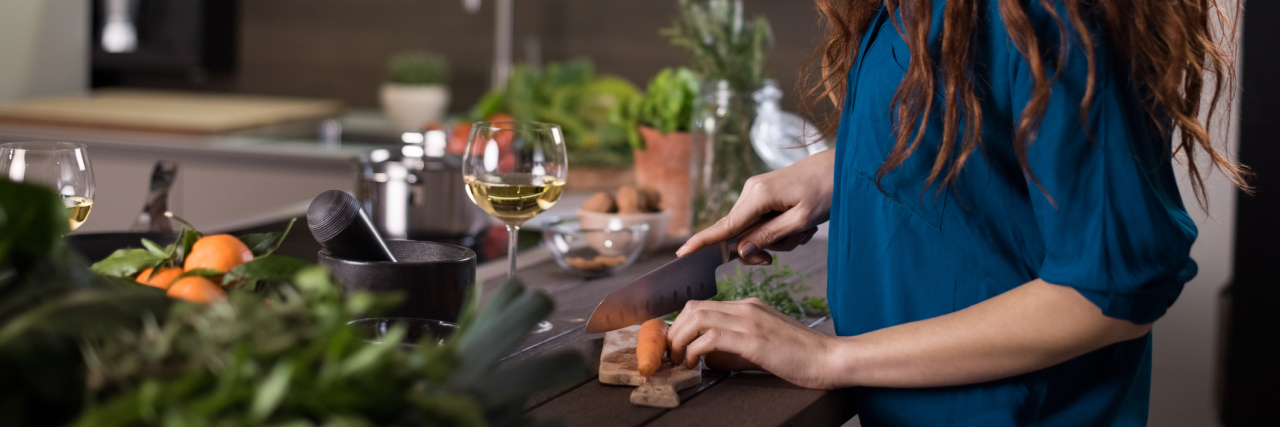 7 Challenges for Eating Healthy When You're Chronically Ill A woman cutting a carrot in the kitchen, cooking a meal.