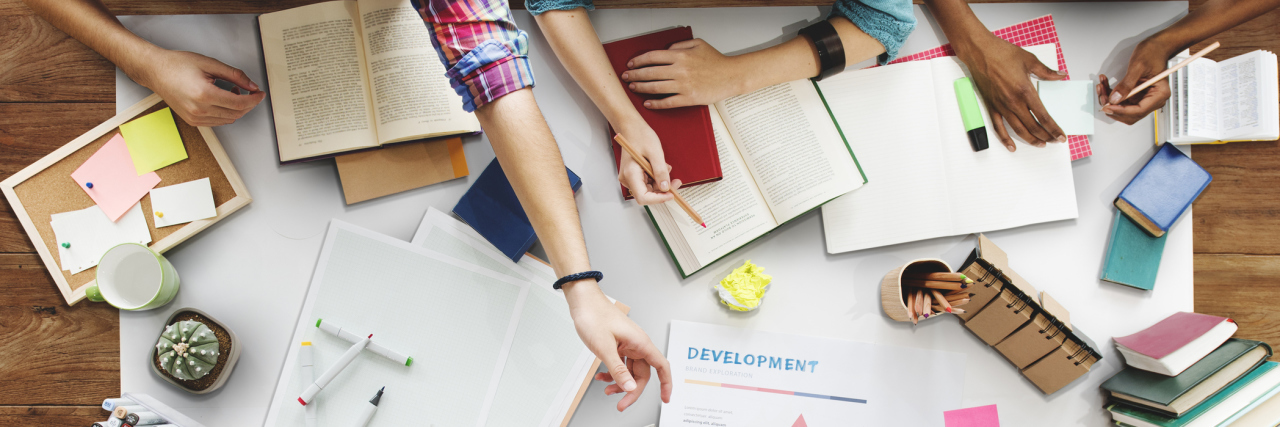 7 Things I Want My College Classmates to Know About My Gastroparesis A table of text books, and showing college students arms on top of the books - from the edge of the table.