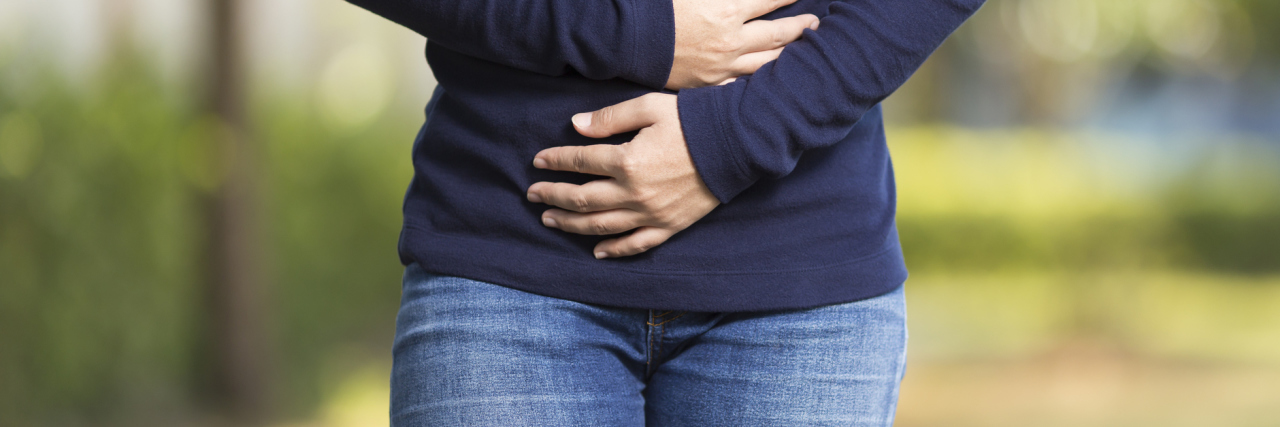 woman in park with stomach ache hands on stomach