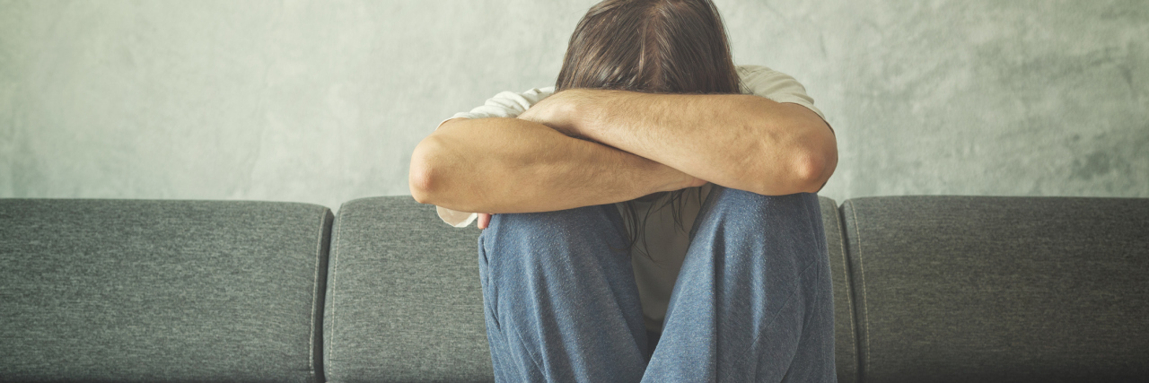 How I Hid My Demon: Possessed by Alcoholism man with depression sitting on sofa cross armed and face buried in arms
