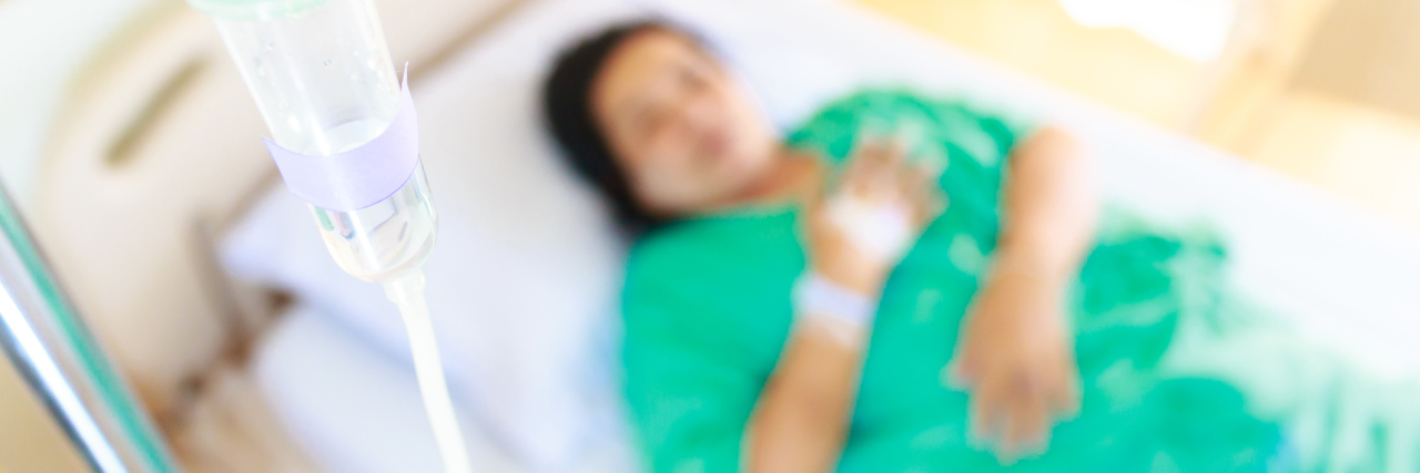 A woman in a hospital bed, focused on an IV of fluids.