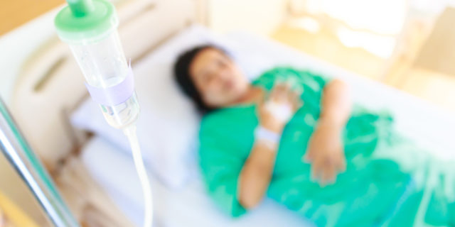 A woman in a hospital bed, focused on an IV of fluids.