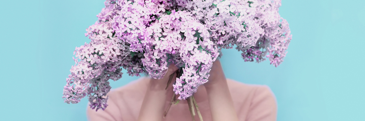 woman hiding her face behind a bouquet of purple flowers