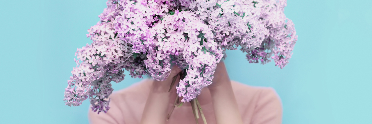 Pretending to Feel Well When You Have Fibromyalgia, Chronic Illness woman hiding her face behind a bouquet of purple flowers
