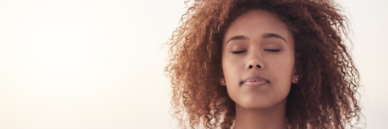 An African American woman standing at hte beach with her eyes closed.