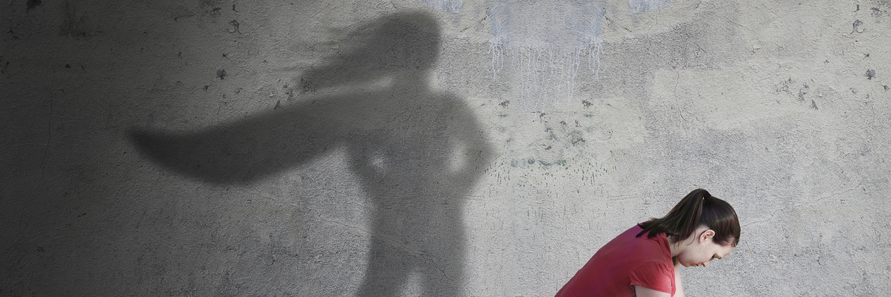 A woman kneeling, with a superhero shadow.