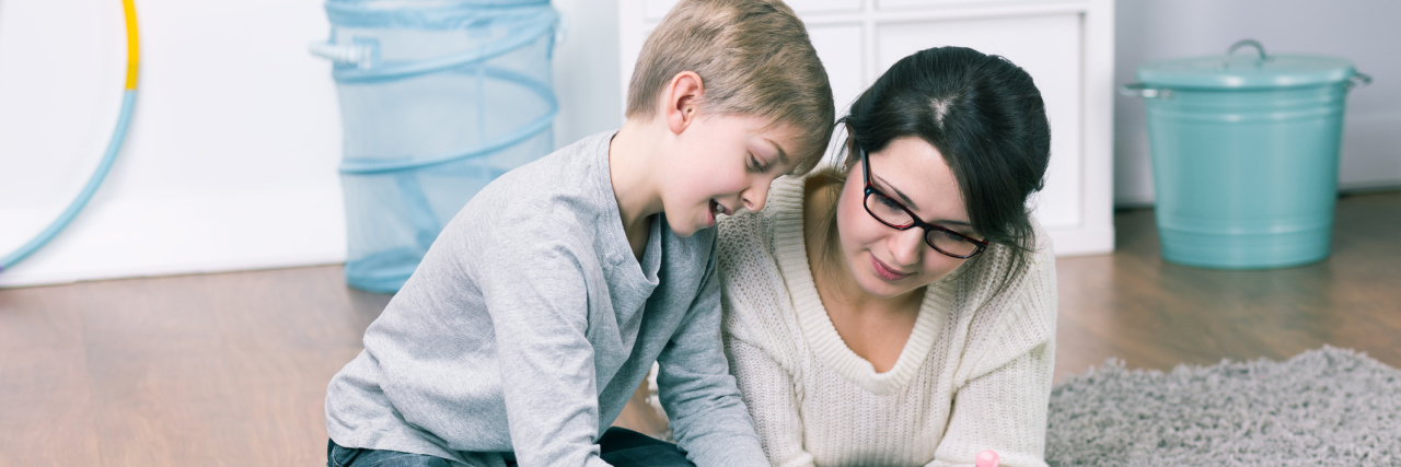 A mom drawing on a chalk board with her young son.