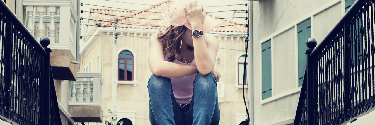 sad woman sitting alone on steps hiding face looking away