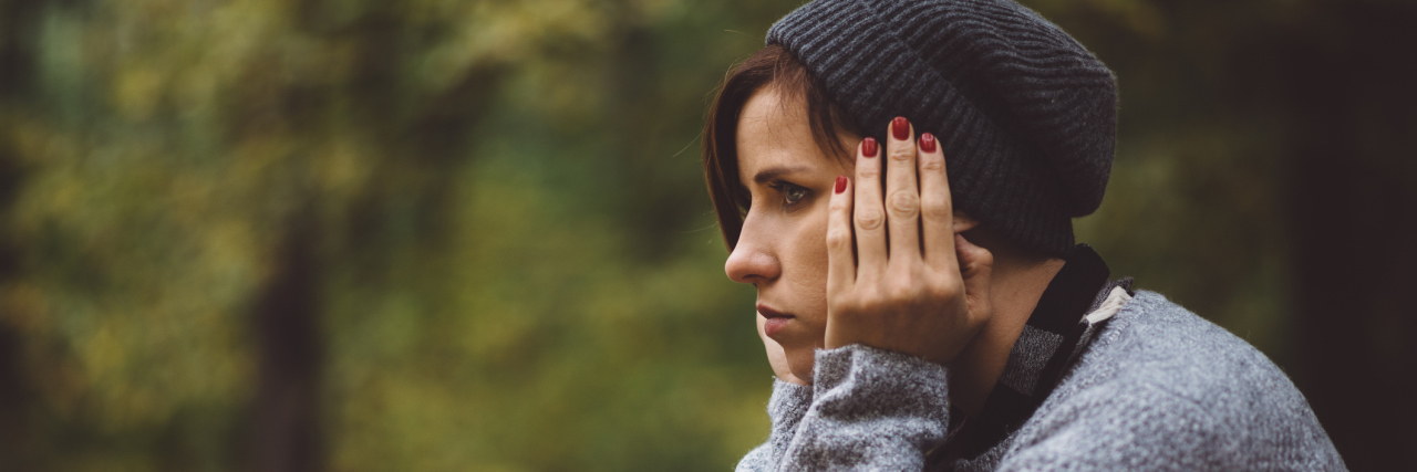 Portrait of sad, depressed woman sitting alone in the forest. Solitude or depression concept. Millenial dealing with problems and emotions.