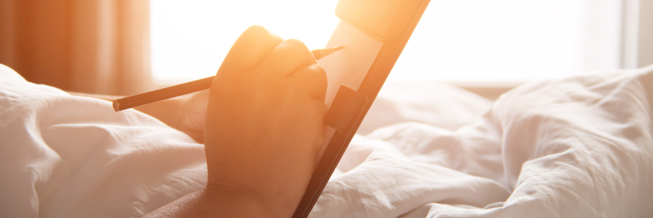 Mistakes I'm Learning From Living With Anxiety woman with notepad and pen writing in bed in warm sunlight