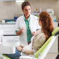 Female dentist in dental office talking with female patient and preparing for treatment.
