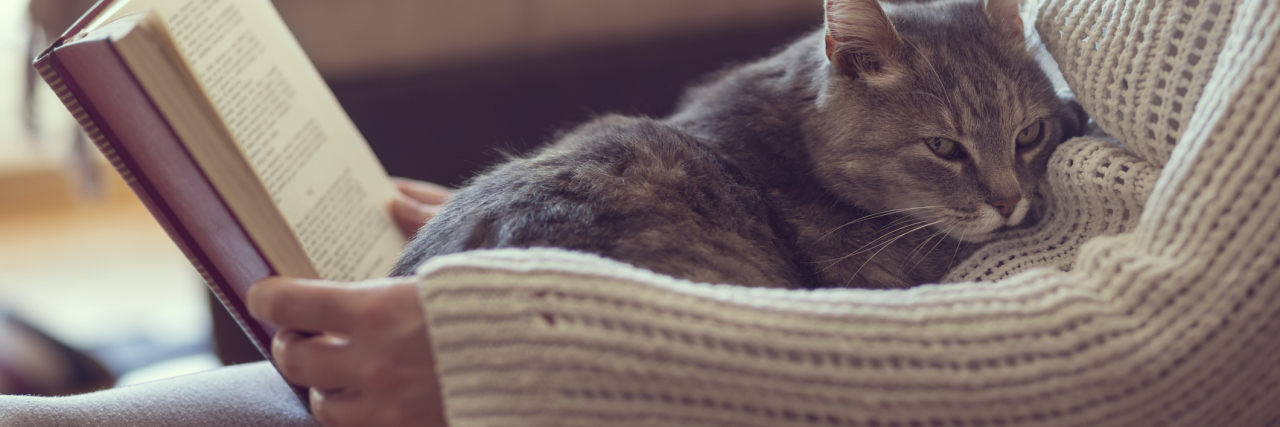 Fibromyalgia: Practicing Self-Care With Chronic Illness woman reading with a cat curled up on her lap