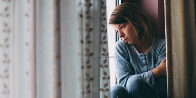 Young sad woman sitting on the window looking outside