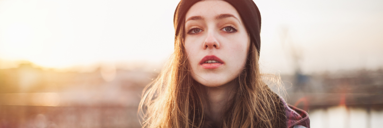 UCTD: How Feeling Invisible Inspires Me to Make My Illness Visible woman in a beanie standing outside at sunset