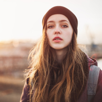 woman in a beanie standing outside at sunset