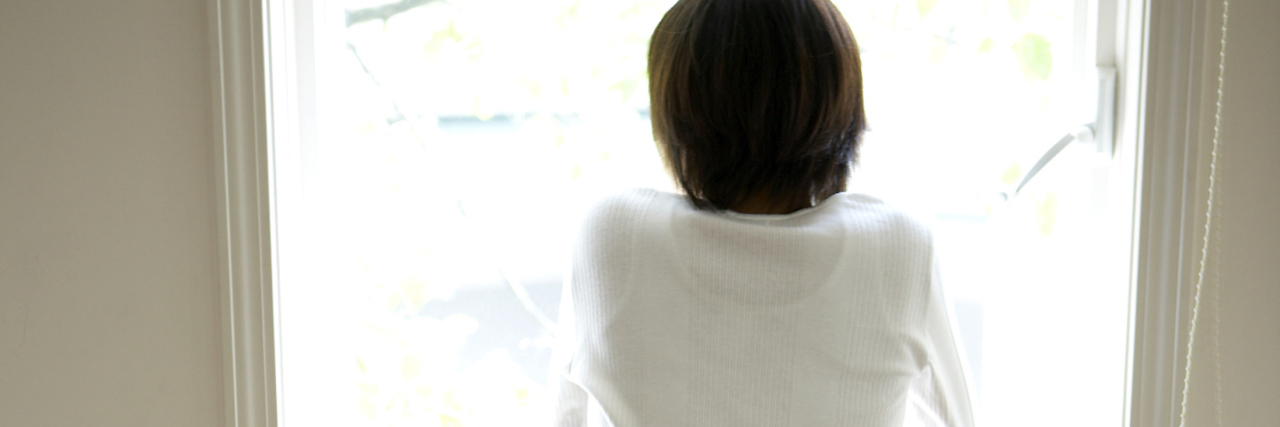 When Things Need to Be Pushed Back for My Health to Come First Woman looking out of window in home, rear view