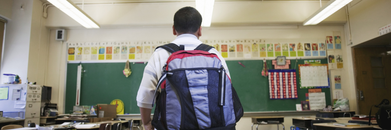 Addressing Chronic Back Pain in Children Boy wearing backpack in classroom.