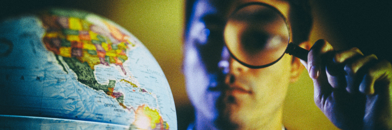 Man looking at a globe through a magnifying glass.