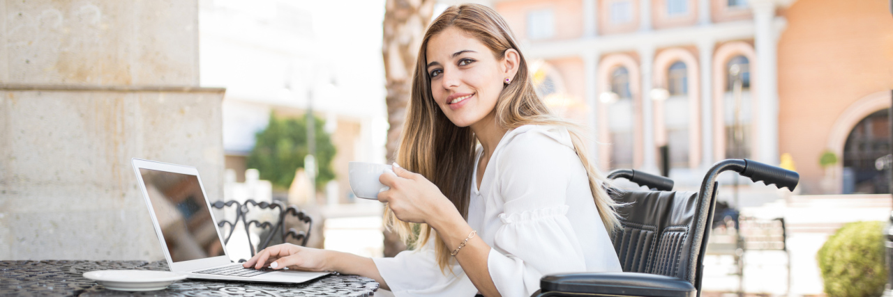 It's Time to End the Stigma Around Mobility Aids A young woman at a cafe, writing on her laptop, as she sits in her wheelchair.