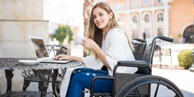It's Time to End the Stigma Around Mobility Aids A young woman at a cafe, writing on her laptop, as she sits in her wheelchair.