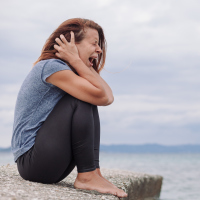 woman with depression alone screaming on bridge with hands over ears