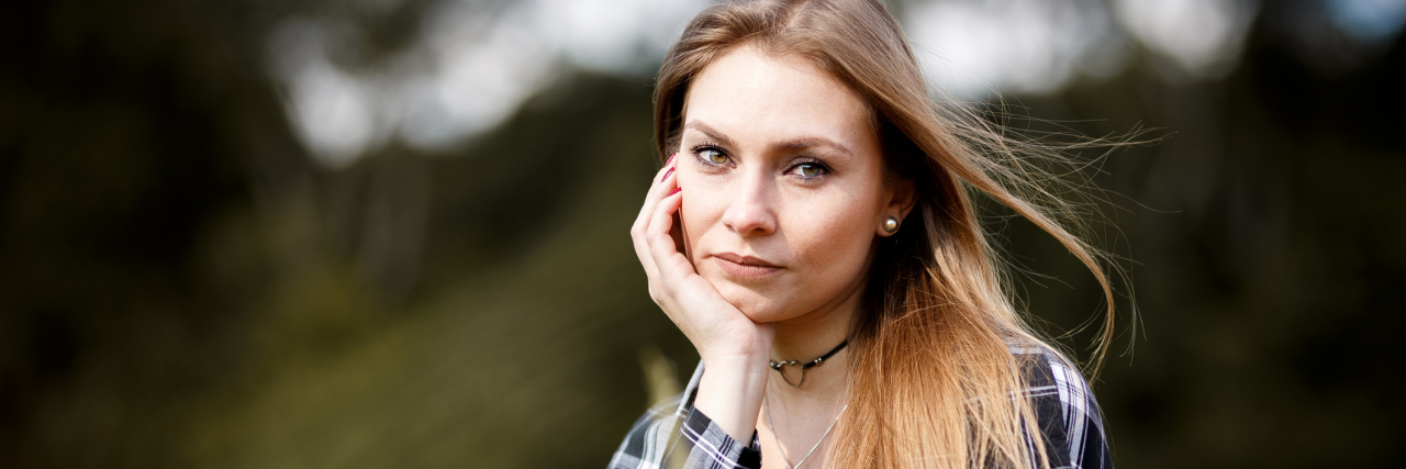 When Doctors Question Our Physical Symptoms Because of Mental Illness A woman in a plaid shirt, outdoors, with a serious expression.