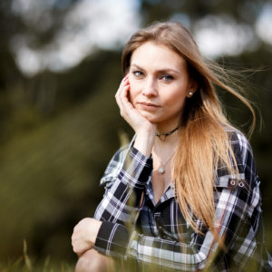 A woman in a plaid shirt, outdoors, with a serious expression.