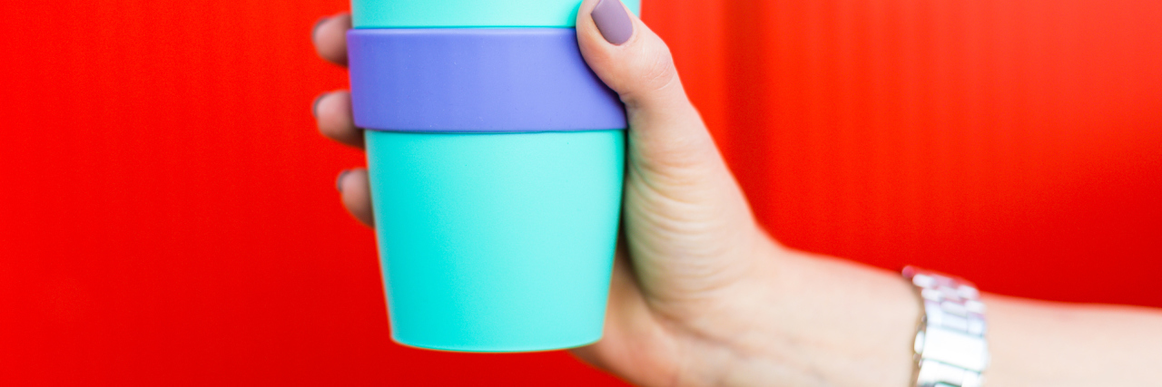 colorful coffee travel mug held against red background by woman