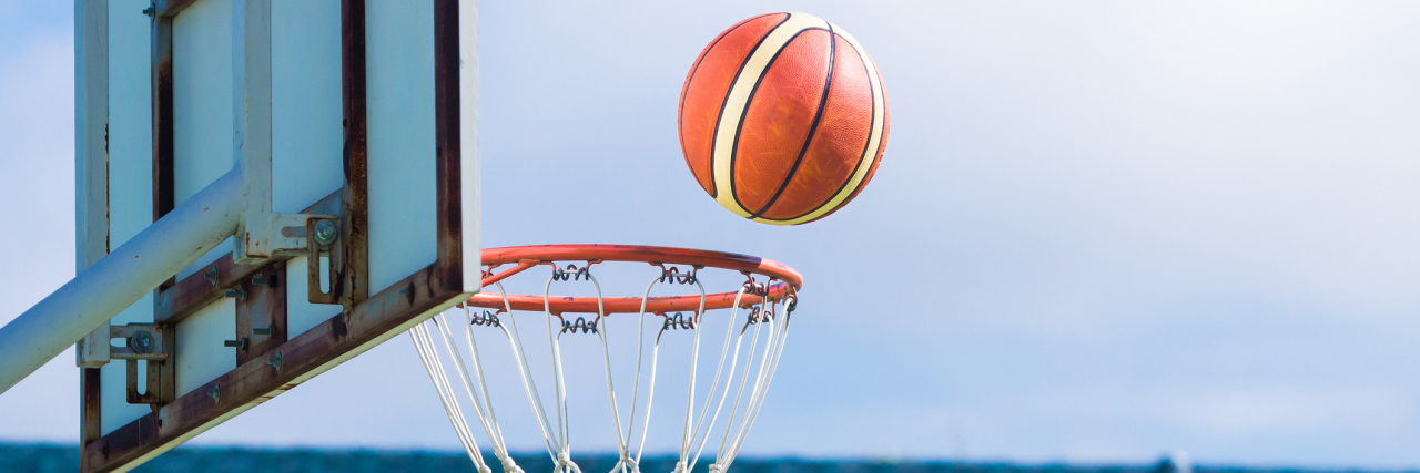 What I've Learned as a 15-Year-Old With Cerebral Palsy Basketball floating about to get in the hoop at an outdoor basketball court.