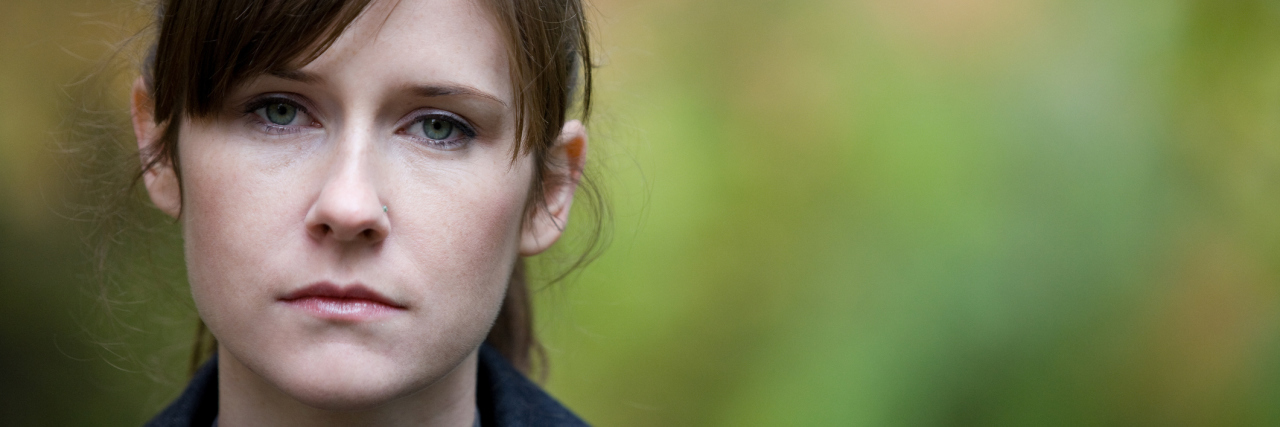 A woman outside, looking at the camera with a serious expression.