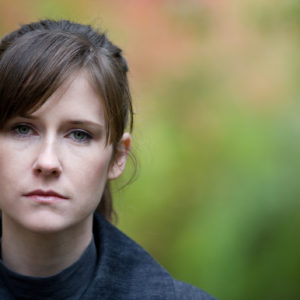A woman outside, looking at the camera with a serious expression.