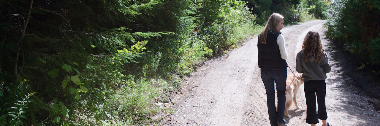 Mother and daughter walking dog on road through forest