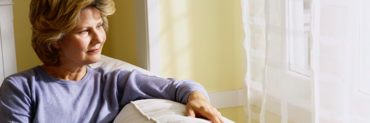 Life With a Rare Disease After Medical Retirement woman sitting on her couch and looking out the window